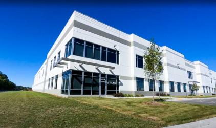 New Felins building stands tall among green grass and a blue sky. The building is white and grey with modern architectural design and large windows.